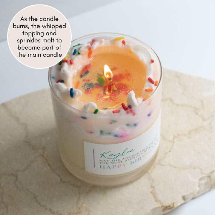 A lit candle labeled Kaylee May the angels sing to you the most joyous chorus of Happy Birthday with whipped cream and sprinkles at the top. Sitting on a granite surface.