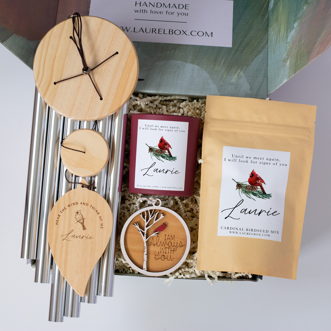 A close-up of a laurelbox gift set with a variety of items, including a birdseed mix, an ornament, a wind chime, and a candle, all personalized with a name and marked with a cardinal design.