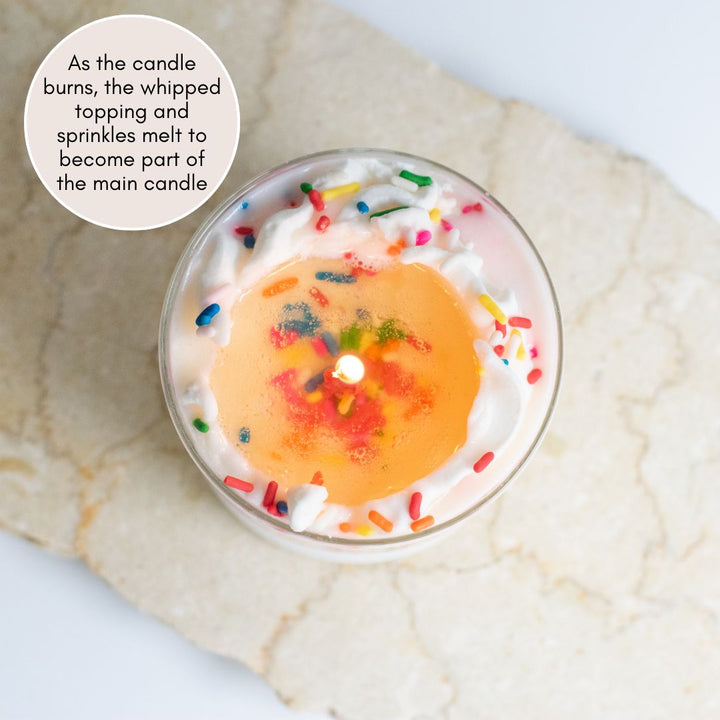 Overshot view looking down at a lit candle with sprinkles resting on a granite surface.