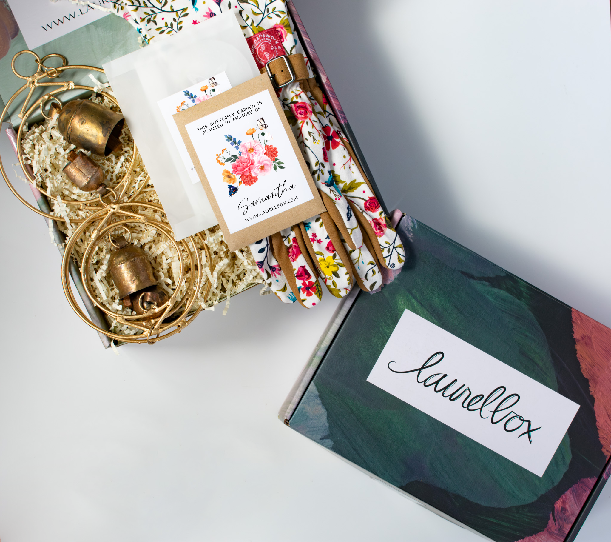Decorative gift box with a floral design on top, filled with a gold wind chime, a personalized seed packet, and floral gardening gloves
