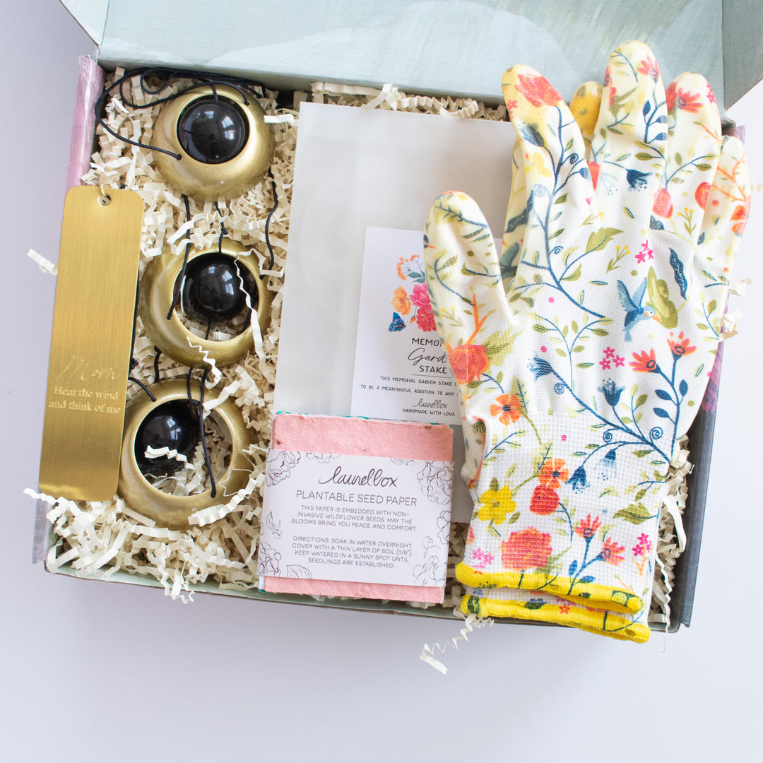 photo of a gift box containing a memorial wind chime, a memorial garden stake, plantable seed paper and floral gardening gloves