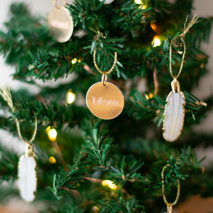 A close-up of decorative gold and white ornaments on a tabletop Christmas tree with blurred lights in the background.