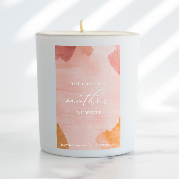 photo of a small white candle with a pink label that displays The Love Of A Mother Is Forever in white writing