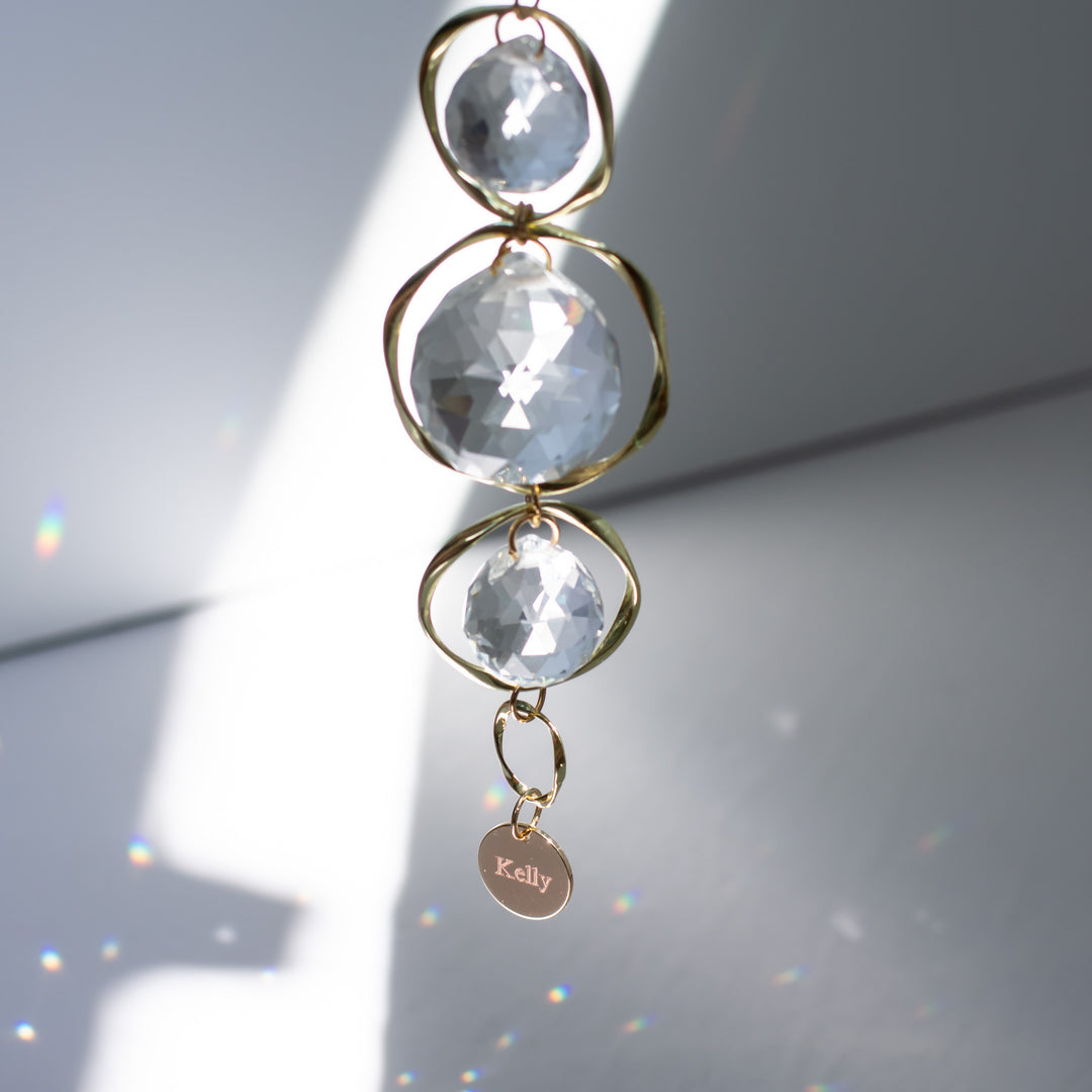 A top view of a custom memorial sun catcher and rainbow maker, featuring an engraved charm at the bottom with the text 'Kelly' against a gray background.