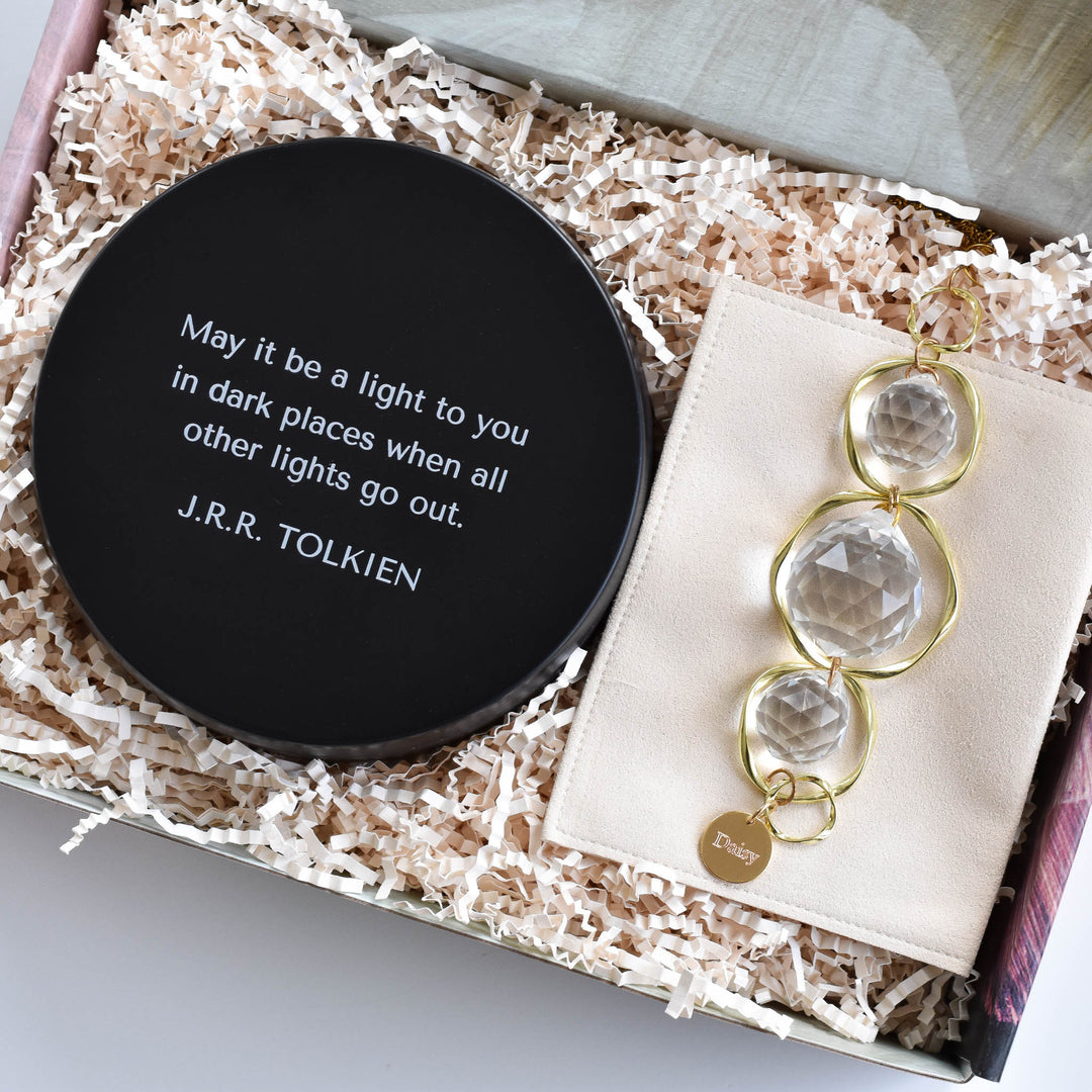 A close-up of an open laurelbox with a candle with a black lid with a quote by J.R.R. Tolkien and a custom memorial sun catcher and rainbow maker with an engraved charm at the bottom with the text Daisy.