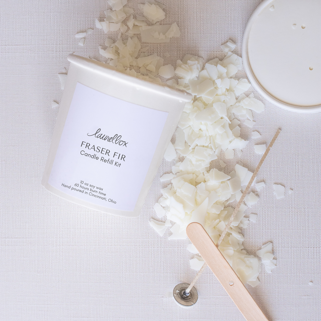 A close-up of an open container of laurelbox's Fraser fir candle refill kit with candle wax scattered across the white background.