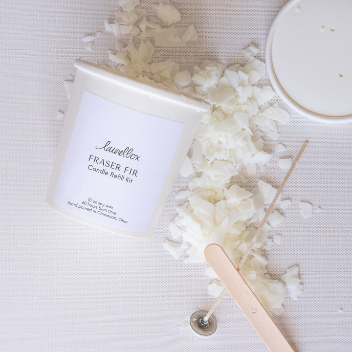 A close-up of an open container of laurelbox's Fraser fir candle refill kit with candle wax scattered across the white background.