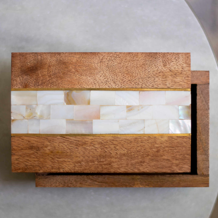 A close-up of a partially opened wooden memory box with mother-of-pearl stones in the middle and placed on a white table.