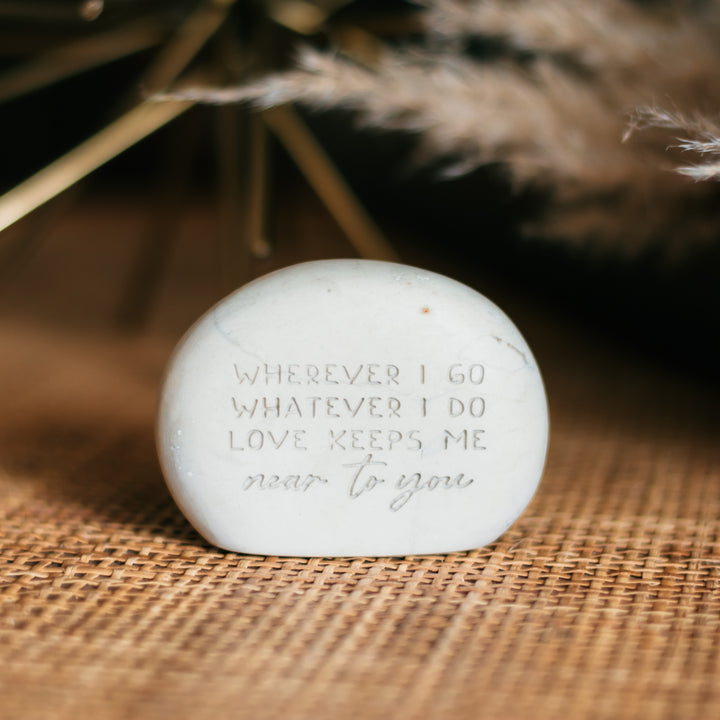 A memorial gemstone with Whenever I Go Whatever I Do Love Keeps Me Near To You engraved on it sitting on a wicker table