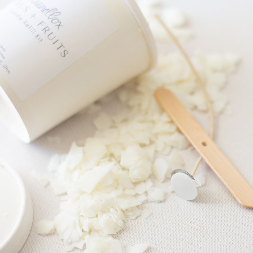 A close-up of a Citrus and Fruits Candle Refill Kit container with scattered wax across the white background and wooden stick