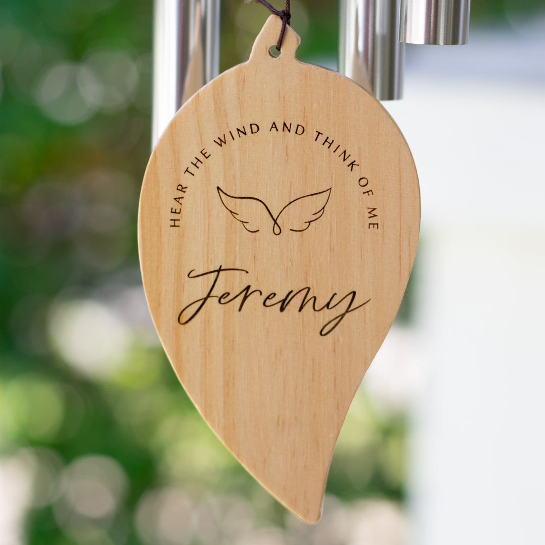 A close up of a wooden leaf is at the bottom of a wind chime with the text Jeremy and Hear the wind and think of me