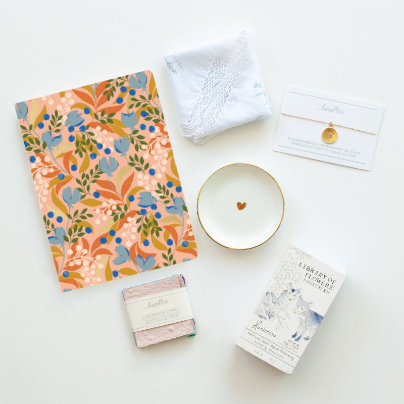 A top view of paper, matches, a handkerchief, a patterned card, a glass tray with a red heart in the middle, a necklace with a handprint pendant scattered against a white background.