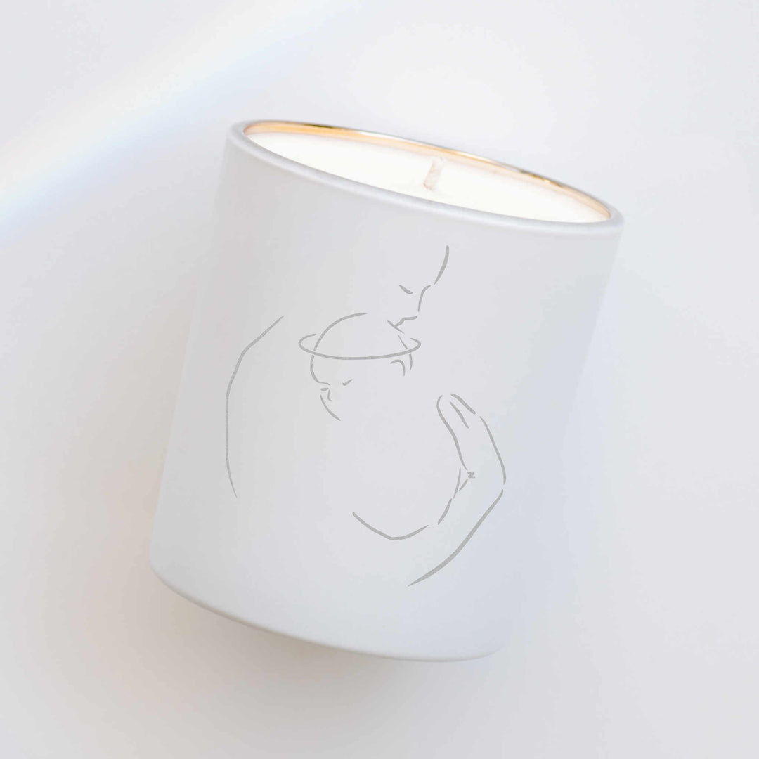 A white-coated candle with an engraved image of a woman holding onto a baby against a white background