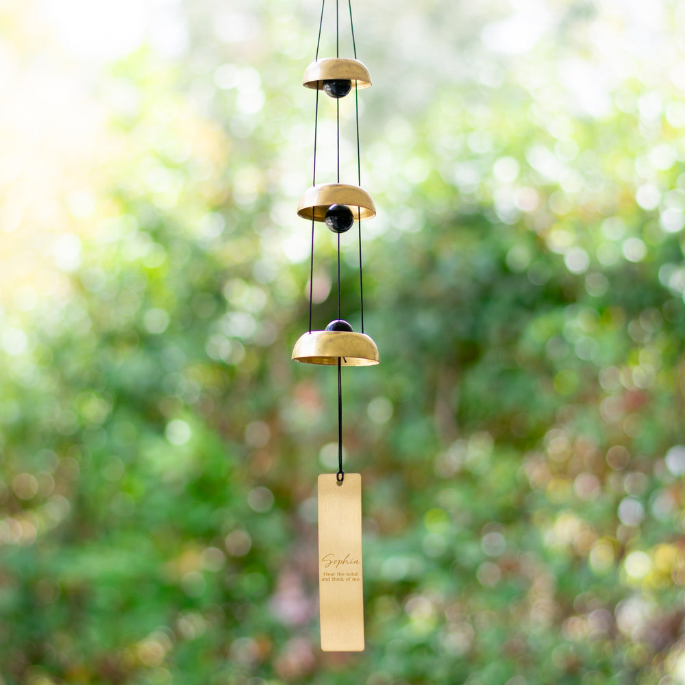 photo of a wind chime made up of a three different sizes of a black ball with a gold circle around it  with a gold rectangle hanging at the bottom