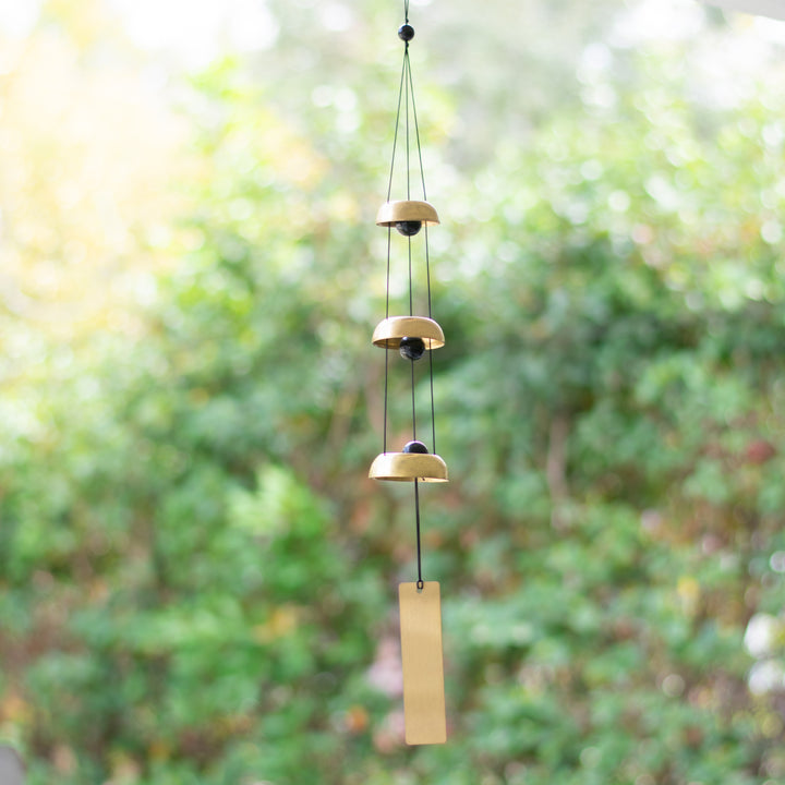 A wind chime hanging outside that features two metallic bells, black cords, and a vertical rectangular tag at the bottom