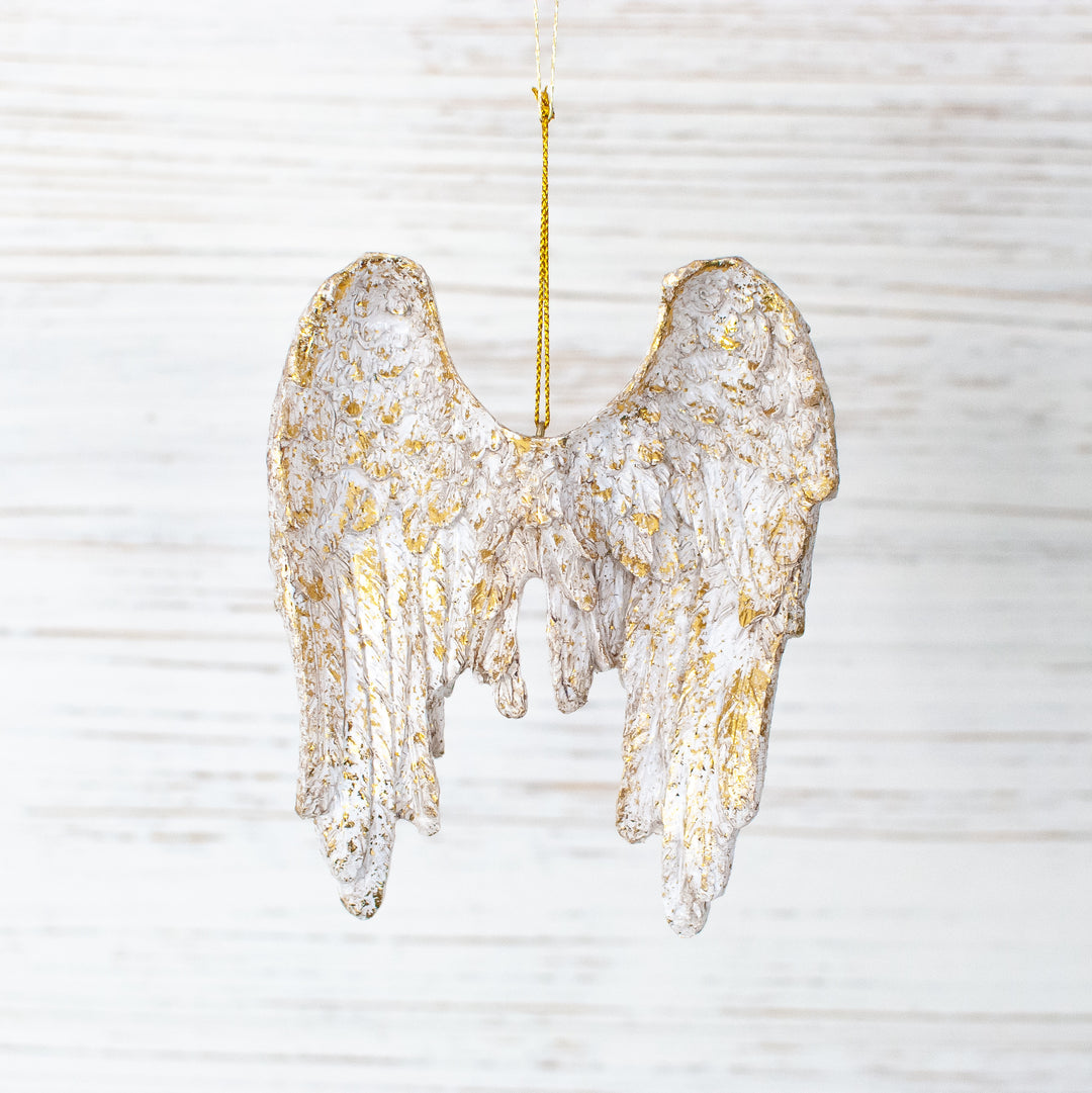 A close-up of an angel wings ornament with gold accents and gold string at the top against a white background.