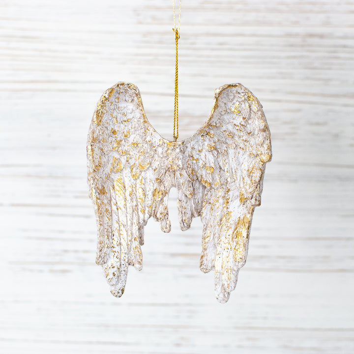 A close-up of an angel wings ornament with gold accents and gold string at the top against a white background.