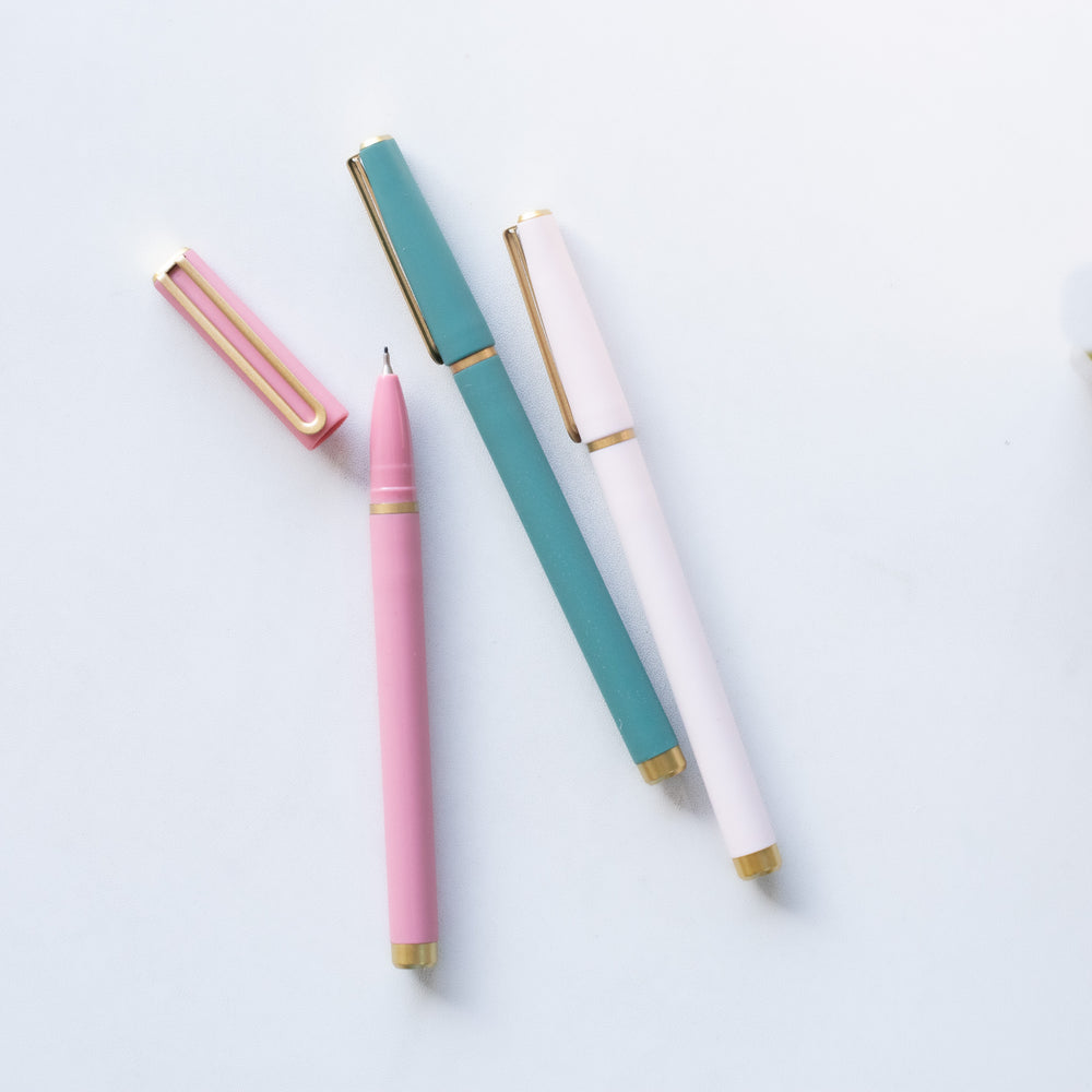 photo of of 3 pens one white, one dark green and one pink - sitting out on a white surface