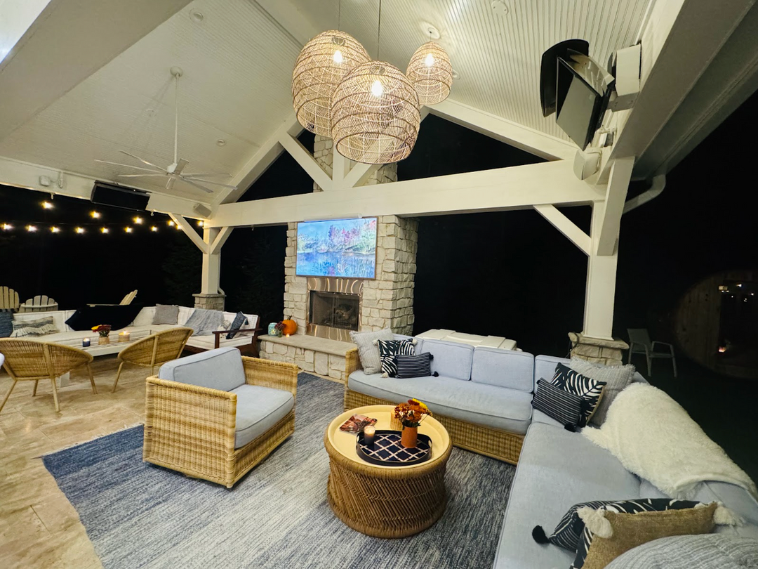 photo of a patio with white beams, a large blue rug with wicker furniture with blue cushions and multi colored pillows on, with other furniture pieces displayed about the patio