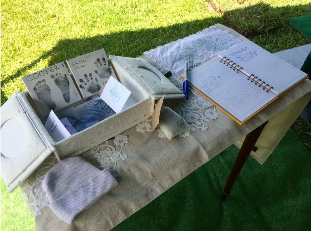 photo of a table set up on green grass with a box filled with various memorial objects next to a book with several notes written in it