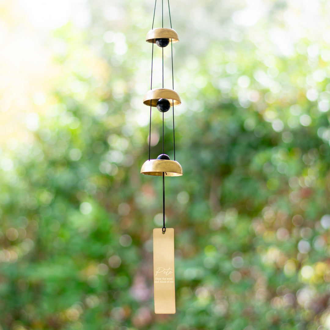 photo of a wind chime made up of a three different sizes of a black ball with a gold circle around it  with a gold rectangle hanging at the bottom
