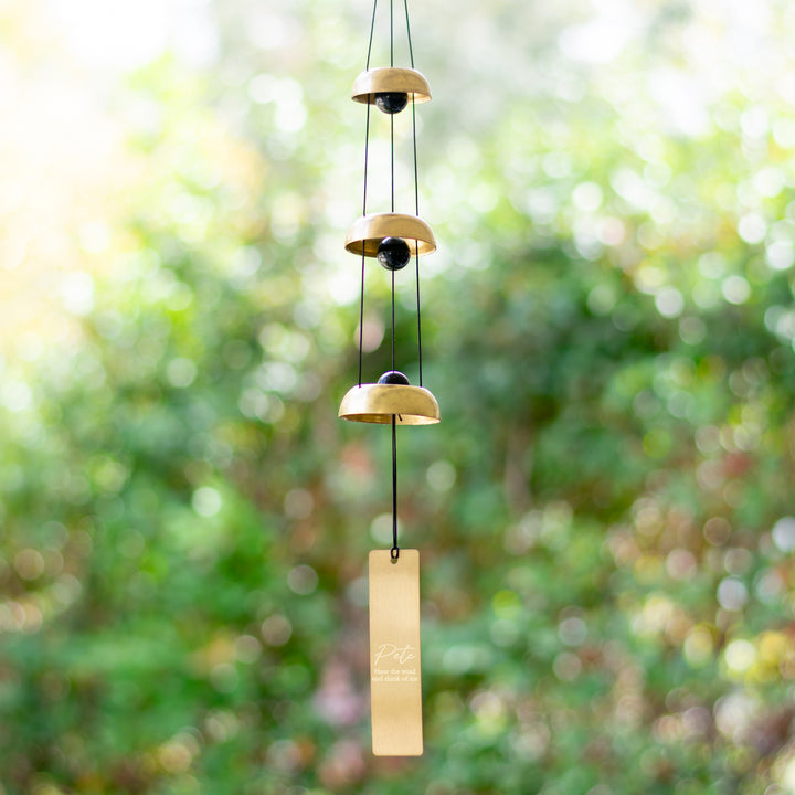 photo of a wind chime made up of a three different sizes of a black ball with a gold circle around it  with a gold rectangle hanging at the bottom