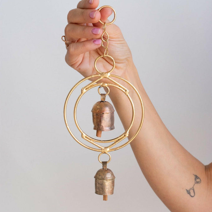 A close-up of a woman holding a gold wind chime with two small bells against a white background.
