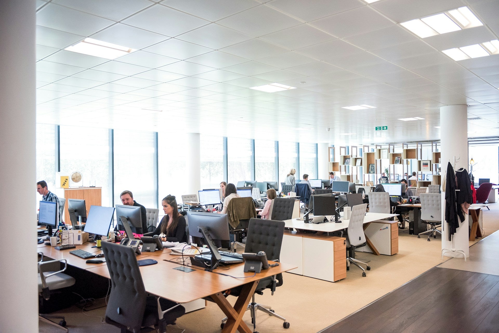 photo of an open office with rows of desks with several computer monitors, key boards and phones on top and several people sitting in chairs at the desks