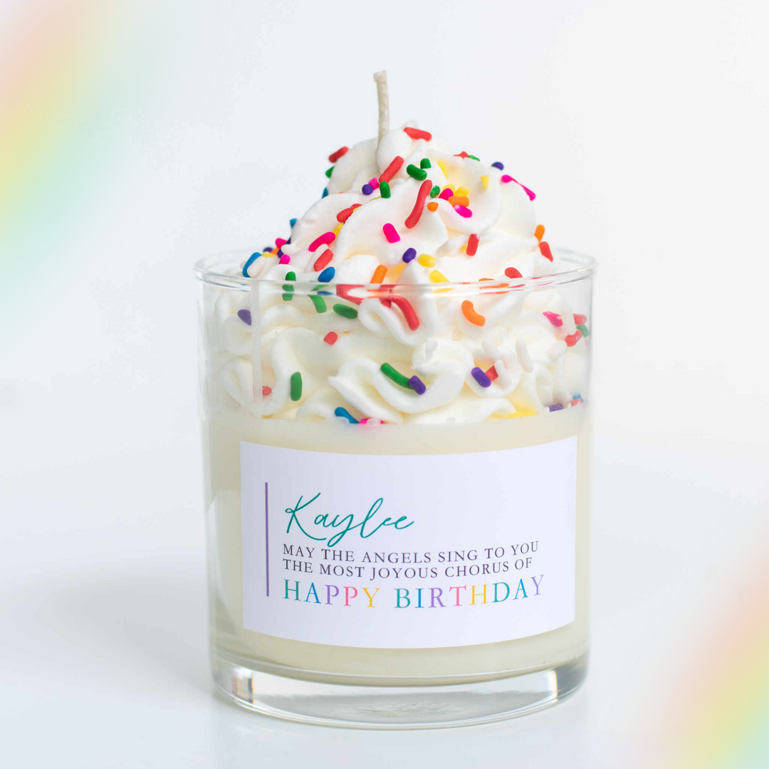 A glass candle labeled Kaylee May the angels sing to you the most joyous chorus of Happy Birthday with whipped cream and sparkles at the top. Sitting on a desk.