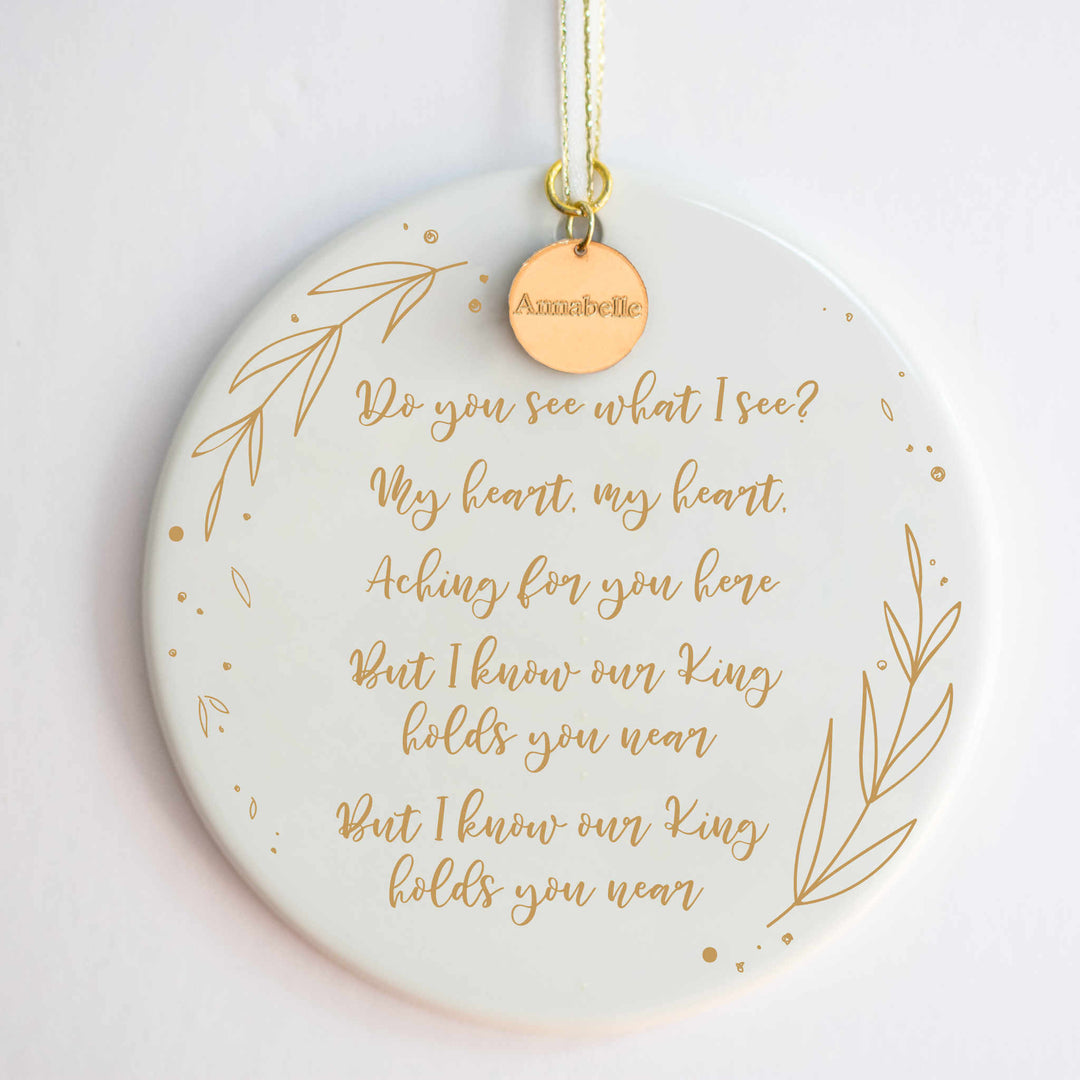 A white ceramic ornament with a "Do You See What I See" carol engraved with gold detailing and a gold "Annabelle" charm at the top against a white background.