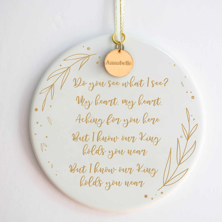 A white ceramic ornament with a "Do You See What I See" carol engraved with gold detailing and a gold "Annabelle" charm at the top against a white background.
