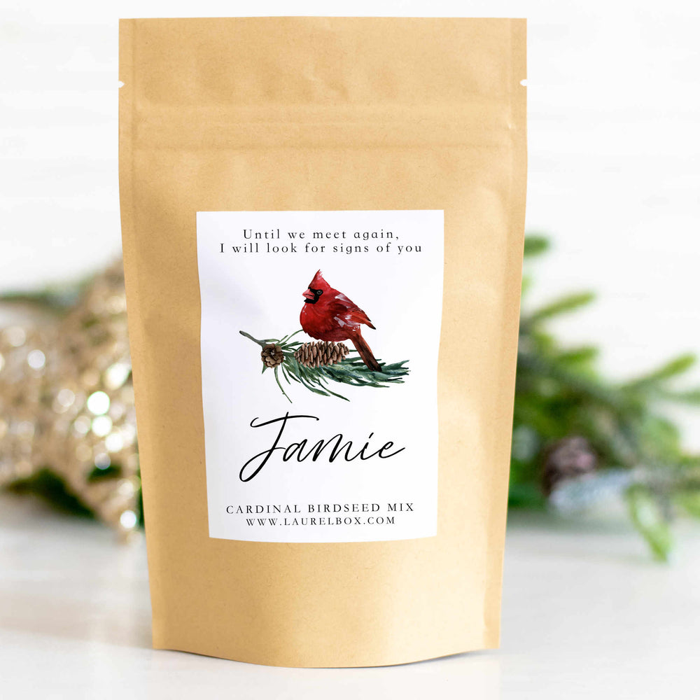 A close-up of a yellow bag with a white sticker that has a cardinal sitting on pine needles and pinecones with the text Jamie below it.