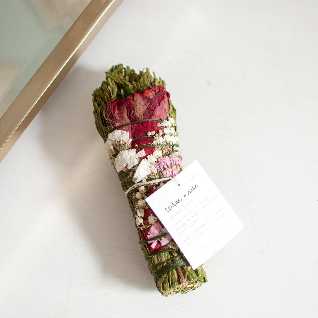A close-up of a bouquet of dried herbs and flowers tied with green string angled to the left, sitting next to a gold-framed mirror.