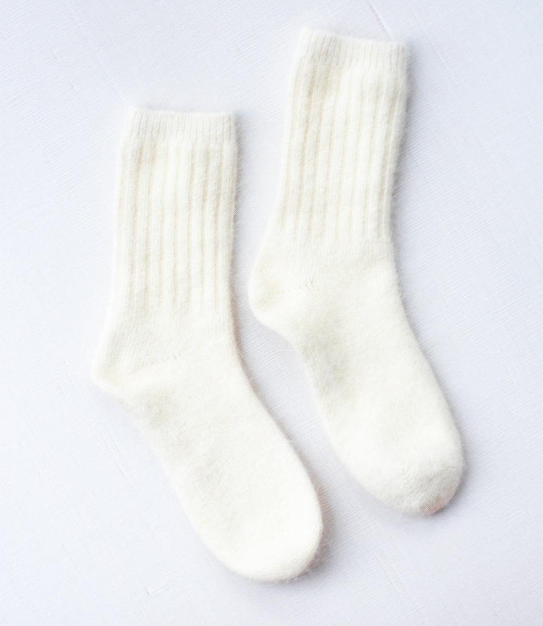 A pair of tall white wool socks against a white background.
