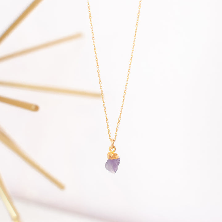 photo of a gold chain necklace with a purple raw cut stone hanging at the end