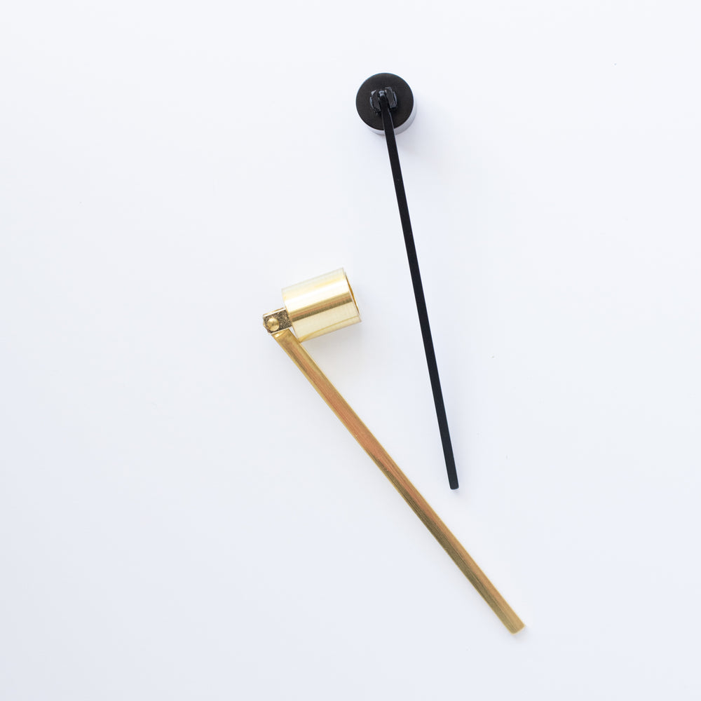 A black and gold candle snuffer scattered on a white surface. Gold candle snuffer on the left and black snuffer laying face down