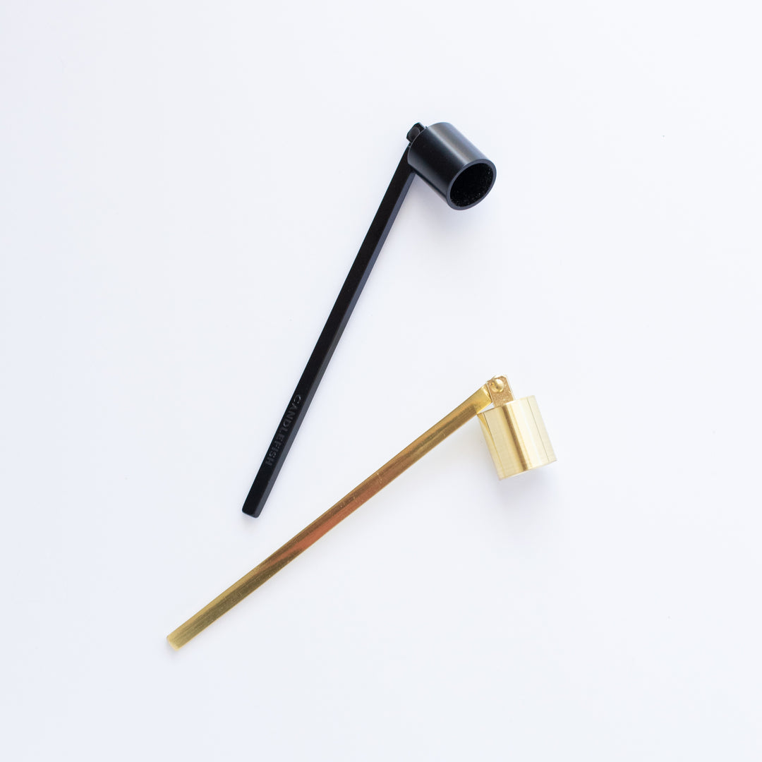 A black and gold candle snuffer scattered on a white surface.