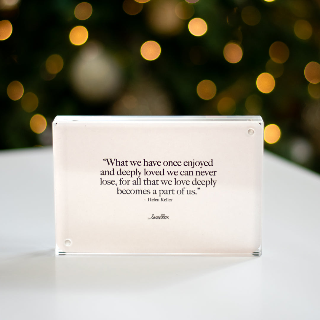 A close-up of a clear, thick panel frame on a white surface with a Christmas tree with lights in the background.