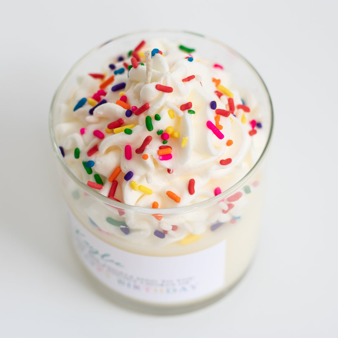 Overshot view of a glass candle labeled Kaylee May the angels sing to you the most joyous chorus of Happy Birthday with whipped cream and sparkles at the top.