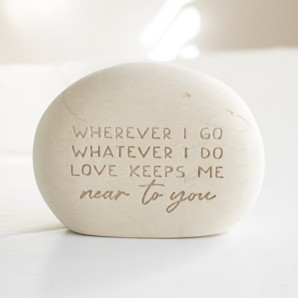 A memorial gemstone with Whenever I Go Whatever I Do Love Keeps Me Near To You engraved on it sitting on a white surface