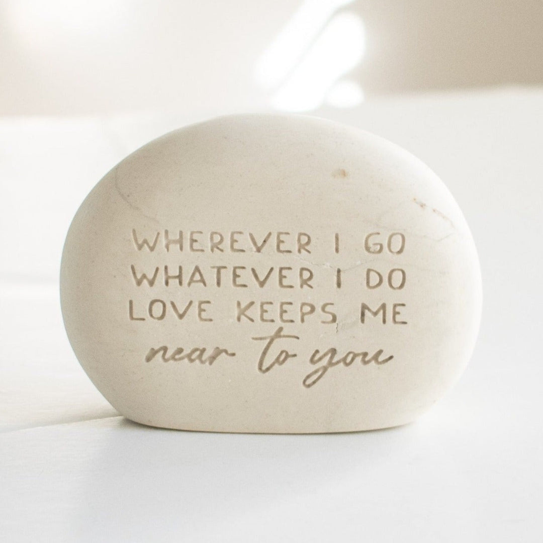 A memorial gemstone with Whenever I Go Whatever I Do Love Keeps Me Near To You engraved on it sitting on a white surface