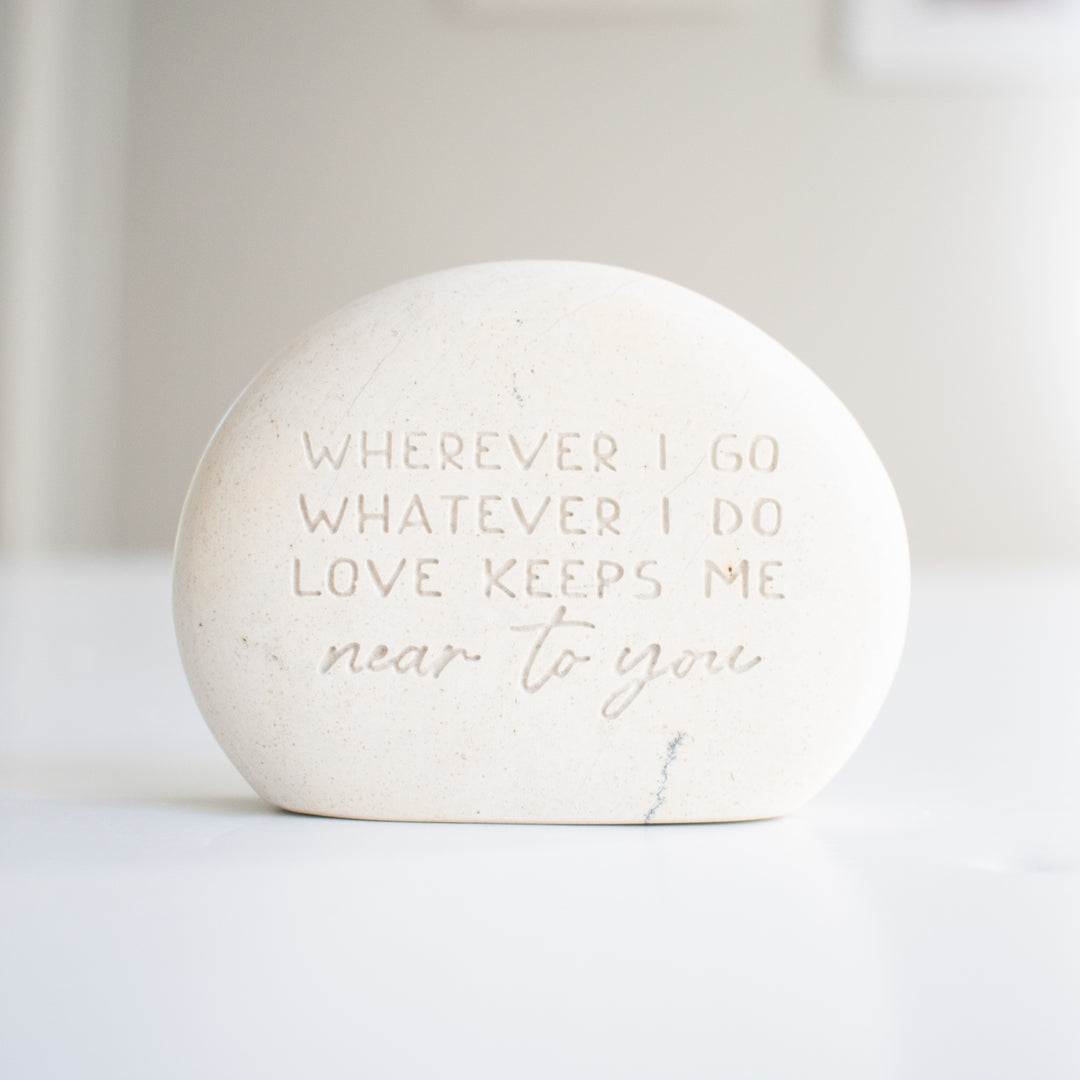 A memorial gemstone with Whenever I Go Whatever I Do Love Keeps Me Near To You engraved on it sitting on a white surface