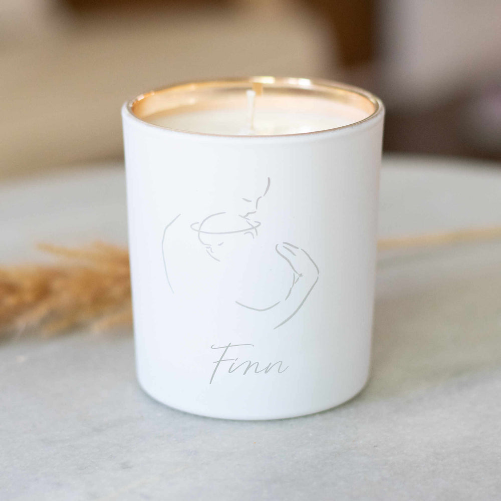 A white-coated candle with an engraved text Finn and image of a woman holding onto a baby  sitting on a granite surface