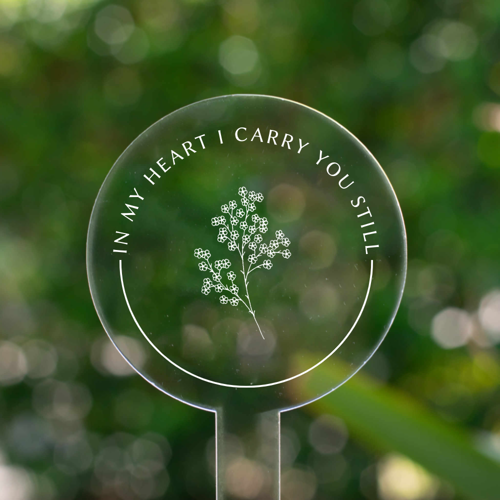 photo of a clear circular garden stake that displays a flower at the center and the words "In My Heart I Carry You Still" around the flower