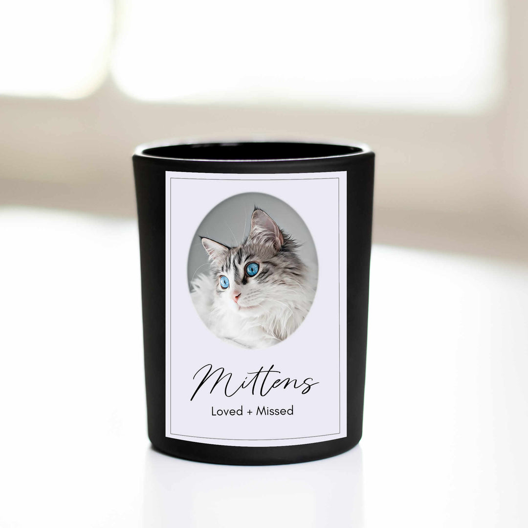 A black-coated candle with a white sticker including the text Mittens we love you and a picture of a cat sitting on a white surface