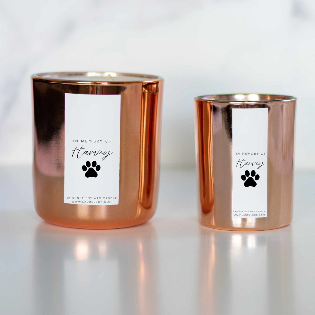 Two gold-coated candles with white stickers, the text In Memory of Harvey, and a paw print. One bigger and one thinner smaller one on the right