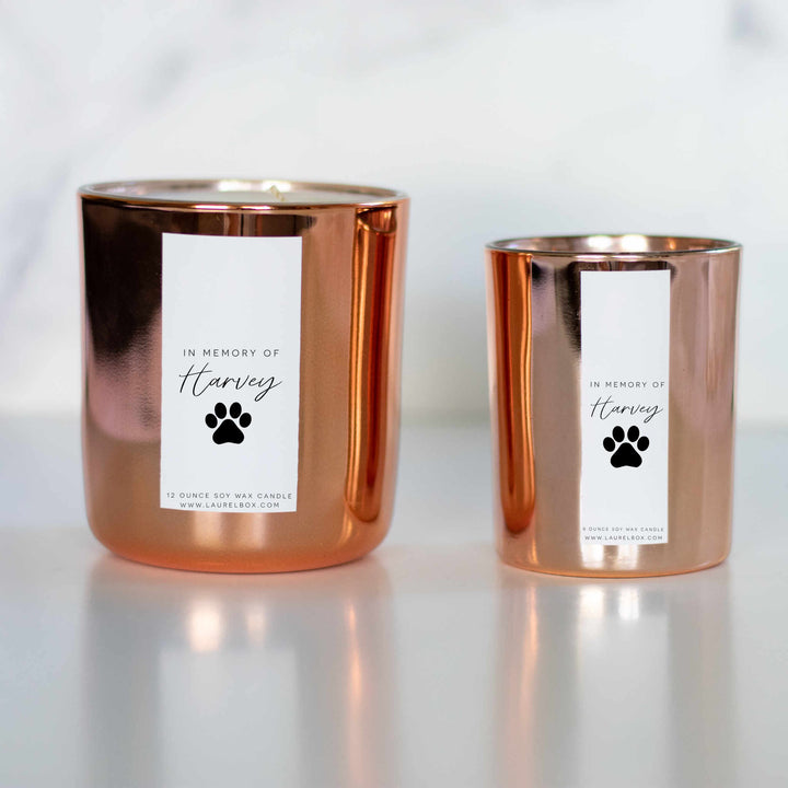 Two gold-coated candles with white stickers, the text In Memory of Harvey, and a paw print. One bigger and one thinner smaller one on the right