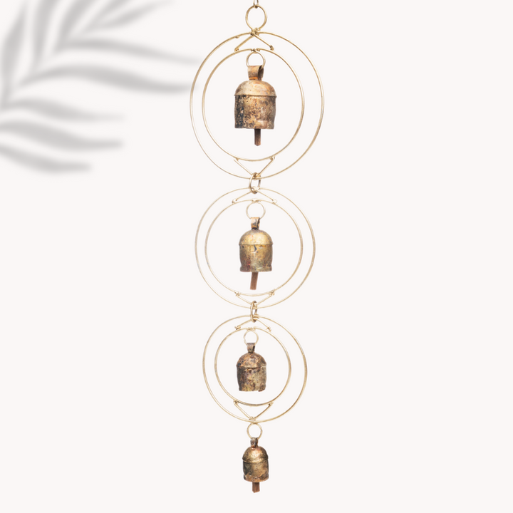 A rustic wind chime of recycled tin and iron coated in copper with four bells with a white background