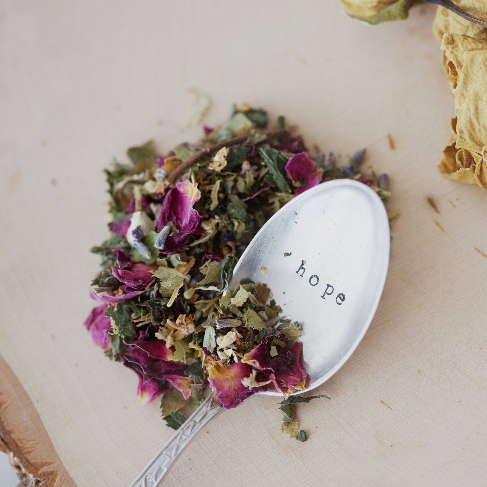 A close-up of a spoon with scattered herbs on a wooden surface
