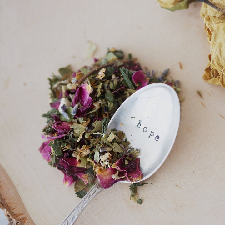 A close-up of a spoon with scattered herbs on a wooden surface